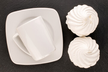 Two sweet white marshmallows with ceramic saucer and cup on slate stone, macro, top view.