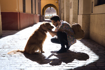 Young Hispanic man with beard and sunglasses crouching with his dog while hugging him on a sunny...