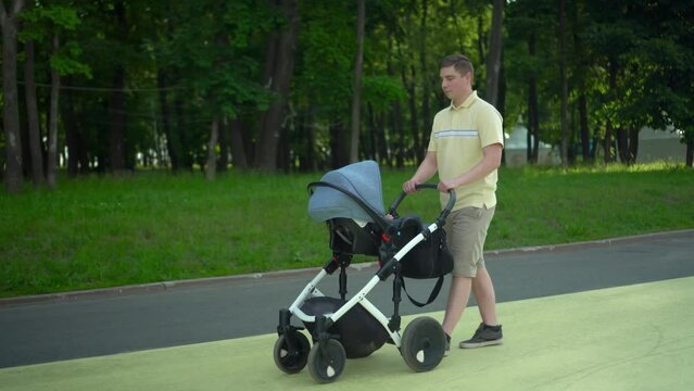 A young man walks with a baby in a stroller