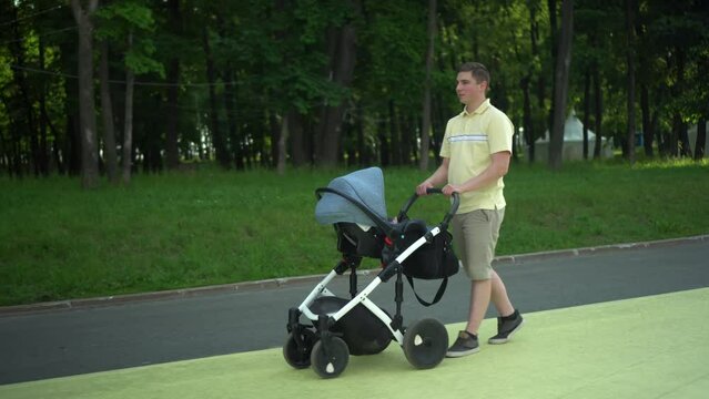 A young father walks with a pram in the park