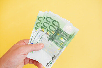 Obraz premium A man holds 100 euro banknotes in his hand on a yellow background. cash paper currency, payment, earning and savings, money and finance concept. Empty space for text