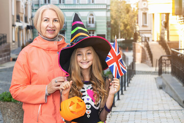 Grandmother and granddaughter with UK flag, near the house on the day of Halloween. Little girl in a witch costume.