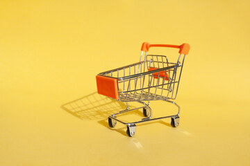 Small supermarket grocery push cart for shopping. Shopaholic. Buyer. Shopping concept. Close-up. Isolated shopping trolley on a yellow background. Copy space.