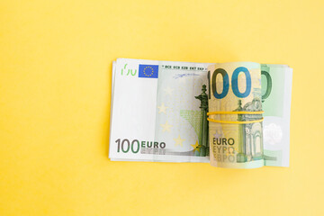 Money roll of euro banknotes with a elastic band on a 100 euro paper bill on a yellow background. cash currency, payment, earnings and savings, the concept of money and finance. Empty space for text
