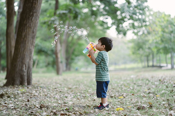 Portrait of Cute little boy blowing bubbles with gun that blows soap bubbles in the park at the day time. Kid plays with soap bubble’s gun outdoor.