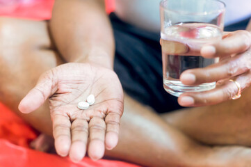 Man with flu or covid 19 holding medicine in hand with a glass of water to take to release headache and illness