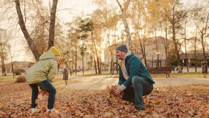 Naklejka na ściany i meble father and little child in an autumn park throw dry leaves up, happy family, live fun with dad, cheerful kid plays with foliage and parent hands throwing leaf fall, parental care of girl, nature walk.