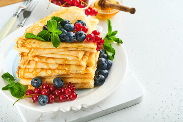 Pancakes. Stack of crepes or thin pancakes with berries, blueberries, red currants, raspberries and honey for breakfast. Homemade breakfast. Copy space. Selective focus.