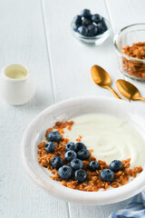 Yogurt. Greek Yogurt with granola and fresh blueberries in white bowl over old white wood background. Morning breakfast concept. Healthy food for breakfast, top view