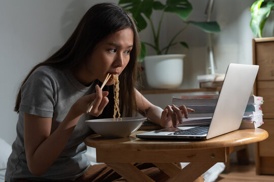 Relaxation, alone smile asian young woman eating instant ramen, noodles while using, watching video, movie, media on pc, tablet and reading news, browsing internet in overtime night, late time at home