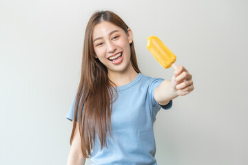 Cheerful enjoy, happy cute asian woman wearing casual with brunette hair, eating popsicle, teenage girl holding ice pop, lolly frozen stick with mango yellow, passion fruit ice cream tasty in summer.