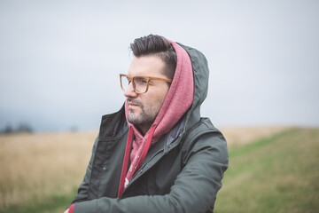 Portrait of an unshaven white man with glasses sitting on a rock on a trail on a foggy day in the mountains.