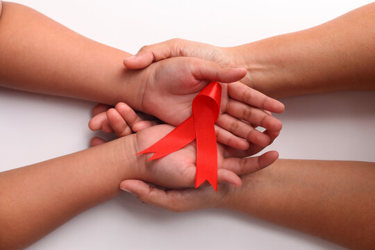 Close up photo of woman's hand and child's hand holding red ribbon together. Aids day concept