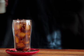 Ice coffee in a tall glass with coffee beans on the table in red plate.