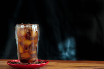 Ice coffee in a tall glass with coffee beans on the table in red plate.