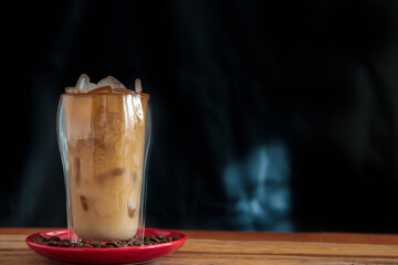 Ice coffee in a tall glass and pouring milk from above with coffee beans on the table in red plate.