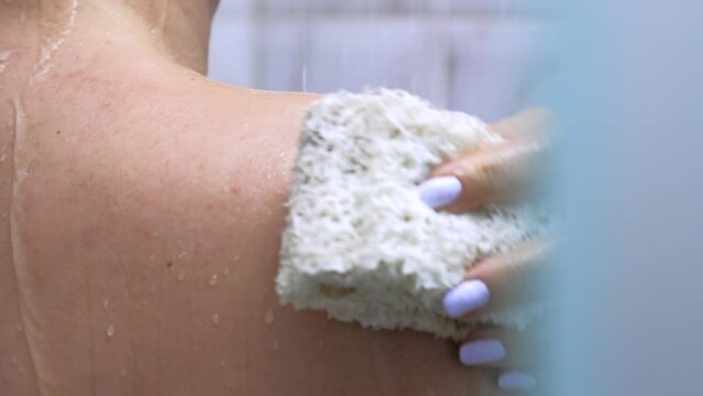 Slender woman holding a soapy washcloth in her hand rubs her shoulders to maintain body hygiene. Woman does hygienic procedures in the bathroom, washes the body with a washcloth with a shower product