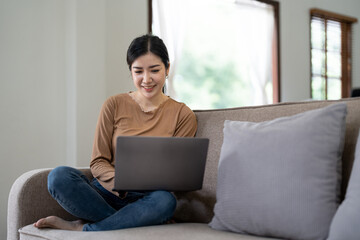 Happy asian woman using laptop in the sofa with a happy face standing and smiling with a confident smile showing teeth