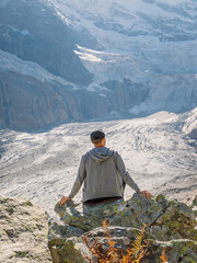 Man sit on rock in the mountains. Mountain with glacier and tourist