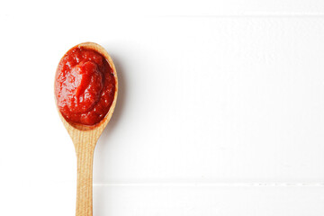 A spoon full of tomato sauce on a white wooden background with space for text. Ingredient Tomato...