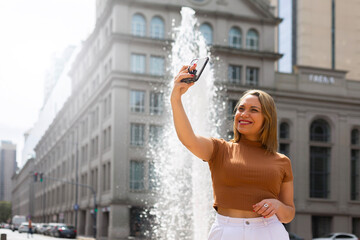 Woman taking selfie with smartphone on background of beautiful fountain in Southamerica. Traveling...