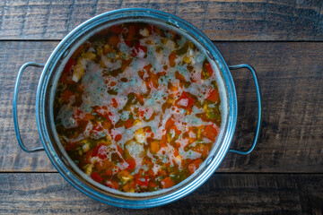 Fresh salmon fish soup with carrots, potatoes and red peppers in a metal pan on wooden table