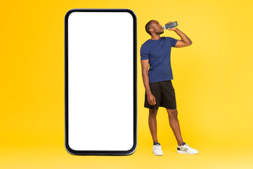 African Guy Near Cellphone Big Screen Drinking Water, Yellow Background