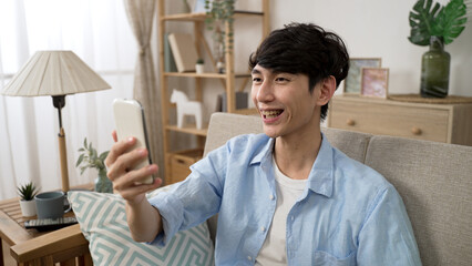 Fototapeta premium cheerful asian Korean man is waving hi and talking with hand gestures while having a video chat with friend on mobile phone during social distancing at home