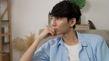 closeup shot of a lonely asian Korean male propping face and gazing into distance in silence while...