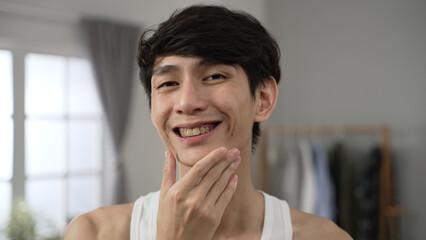 headshot of a satisfied Korean male looking at camera as mirror is nodding head with smile while...
