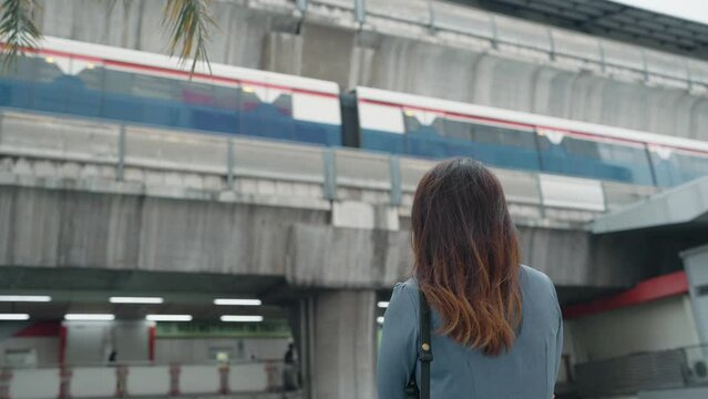 Back view of business woman standing look at BTS sky train, Electric train, running on the way.