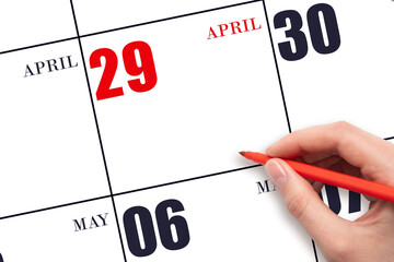 A hand holding a red pen and pointing on the calendar date April 29. Red calendar date, copy space,...