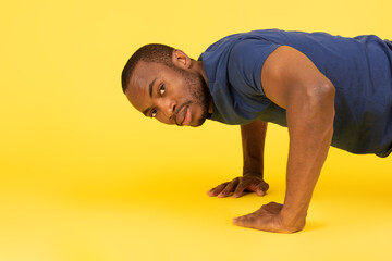 Fototapeta na wymiar Fit Black Man Doing Push Ups Training Over Yellow Background