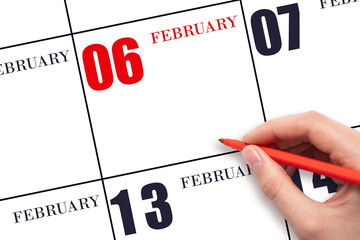 A hand holding a red pen and pointing on the calendar date February 6. Red calendar date, copy...