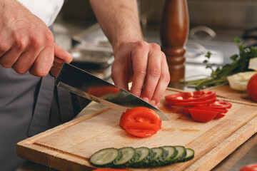 Busy chef cutting tomatoes and cucumbers on a board in modern restaurant kitchen
