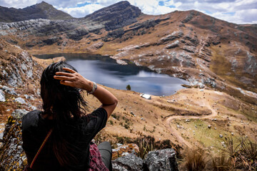 Beautiful native woman contemplates a blue lagoon in the Peruvian Andes.