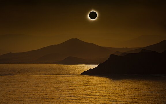 Total solar eclipse in dark red sky above mountains and sea