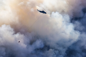 Wildfire Service Helicopter flying over BC Forest Fire and Smoke on the mountain near Hope during a hot sunny summer day. British Columbia, Canada. Natural Disaster