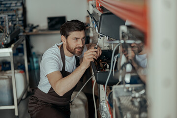 Smiling young man repairing coffee machine using screwdriver in a workshop - obrazy, fototapety, plakaty