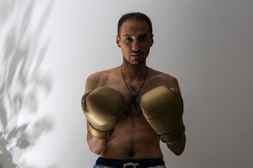 closeup shot of young naked boxer wearing protecting gloves. throwing puches in a boxing ring. grey background © Angelov