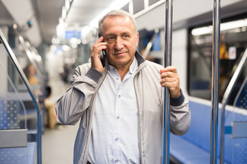 Smiling elderly man using mobile phone in subway car