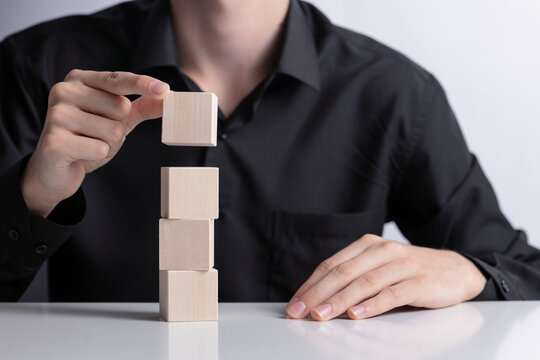 Man's hand completing set of 4 stacked wooden cubes., man build a tower by using four blank wooden cube on table. Mockup for letters, symbol, picture text, word, idea and concept.