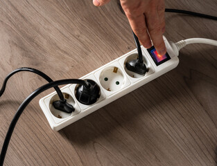 A man cutting off the electrical current by turning off the button on a white electrical socket to...