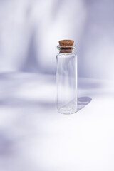  Empty glass miniature bottle with cork cap on contrast shadows background. Still life compositions