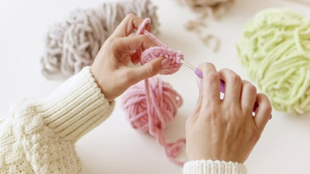 Women's hands knit with crochet hook and woolen fluffy pink threads. Handmade yarn hobby and craft.