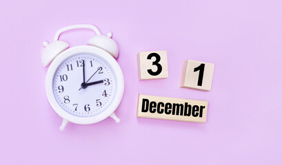 Two wooden cubes and a block with the text DECEMBER 31 and a white alarm clock on a light pink background.