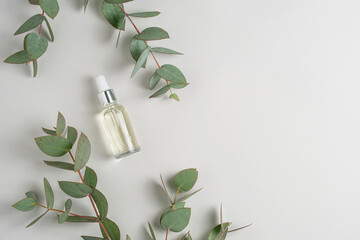 Glass bottle of serum on marble podium and green eucalyptus branches on light grey background top view. Natural layout for cometic product advertising. Copy space for text. Eco concept flat lay.