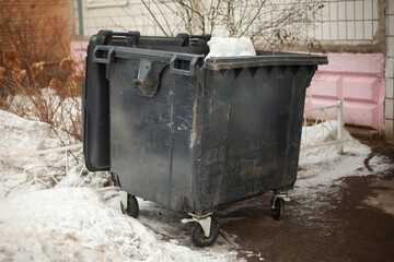 Black garbage can on street. Dirty container in ghetto. Waste garbage.