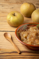 Top view of rustic bowl with cinnamon applesauce on table with pippin apples and wooden spoon, vertical