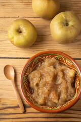 Aerial view of rustic bowl with cinnamon applesauce on table with pippin apples and wooden spoon, vertical